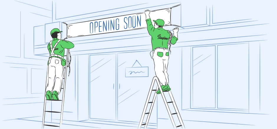 Two construction workers hanging an opening soon banner